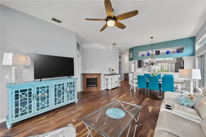 Living room featuring ceiling fan with notable chandelier and dark hardwood / wood-style flooring