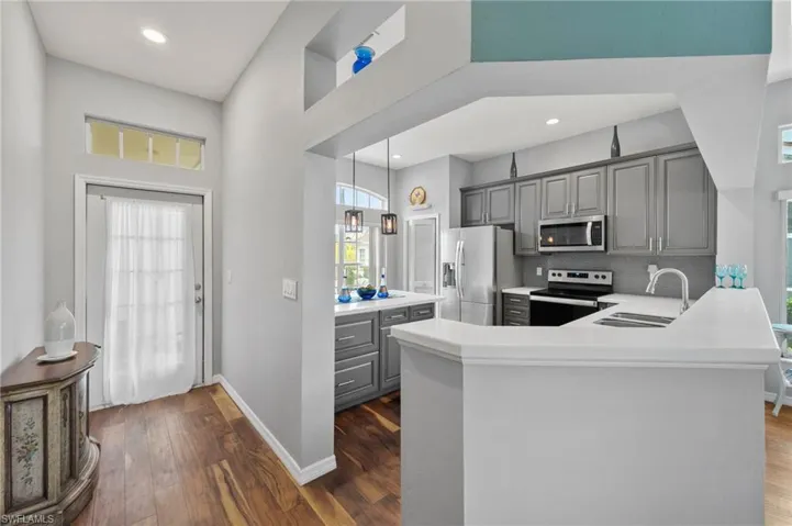 Kitchen featuring dark hardwood / wood-style floors, kitchen peninsula, sink, gray cabinets, and appliances with stainless steel finishes