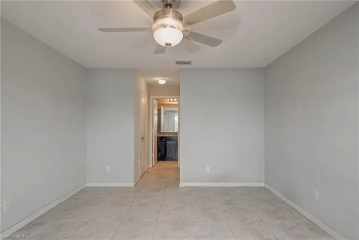 Empty room with light tile patterned floors, visible vents, baseboards, and a ceiling fan