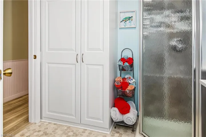 White paneled cabinetry, textured shower enclosure, and hexagonal floor tiling