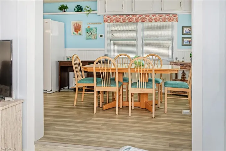 Wood-finish flooring, built-in shelving, white wall paneling, and white kitchen cabinetry