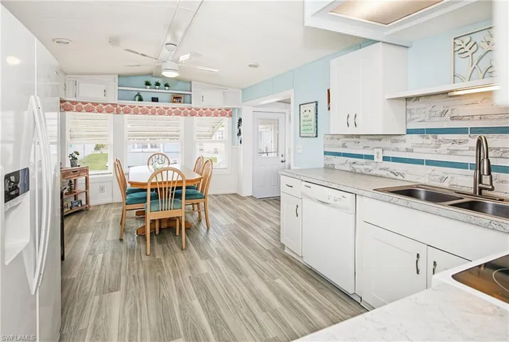 Kitchen featuring white cabinetry, light-toned countertops, a stainless steel double basin sink, and wood-finish flooring