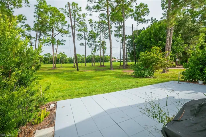 Expansive green space featuring a large patio area, lush landscaping, and mature trees