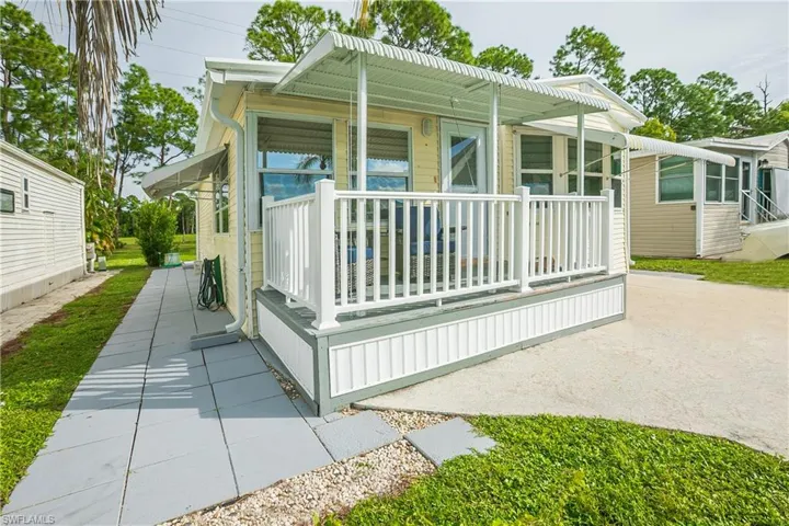 Exterior featuring a covered porch, white railing, corrugated metal awnings, and a concrete paver walkway