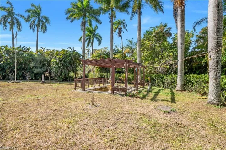 Expansive lawn area featuring a wooden pergola with built-in seating, surrounded by mature palm trees and lush landscaping