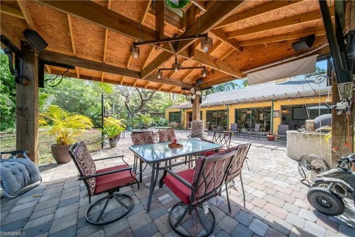 Covered patio with exposed wood beam ceiling, paver flooring, overhead lighting, and built-in outdoor kitchen elements