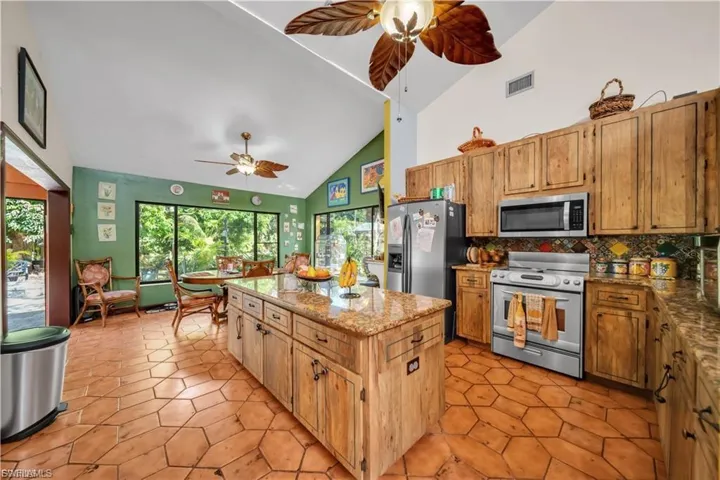 Vaulted ceilings with ceiling fans, wood-finish cabinetry, stainless steel appliances, a granite-top island, and large windows