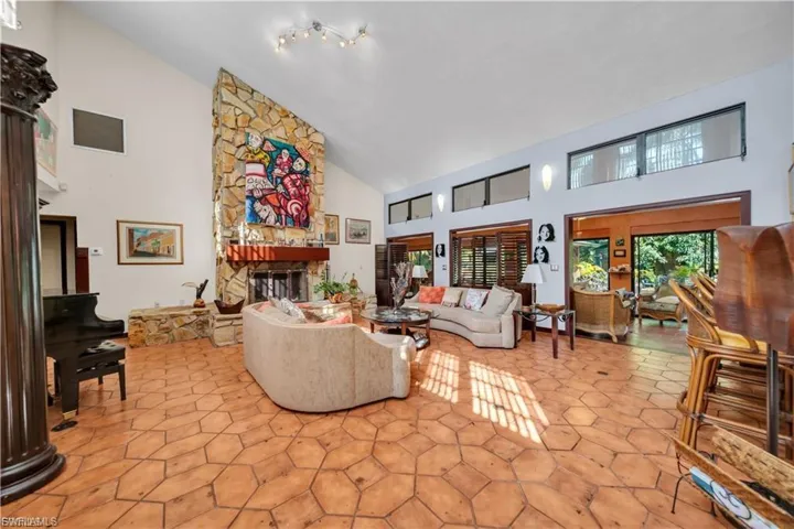 Vaulted ceiling with track lighting, stone fireplace with hearth, and tiled flooring