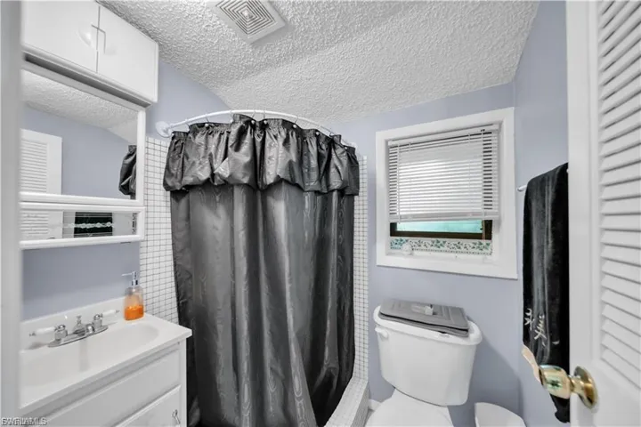 Vanity with built-in storage, shower with tile surround, and a toilet with a window above