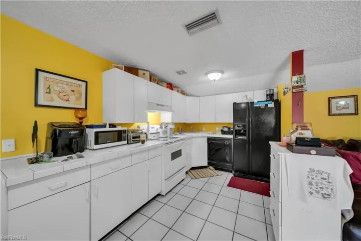 U-shaped kitchen featuring white cabinetry, white tile countertops, white tile flooring, black refrigerator, and black dishwasher
