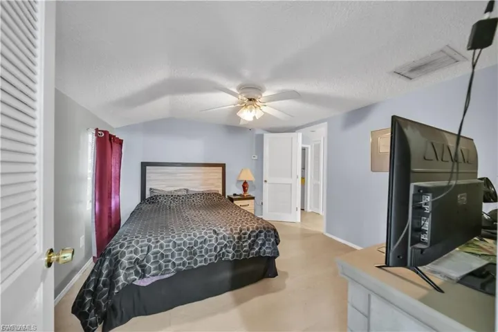 Vaulted ceiling with a ceiling fan, carpet flooring, louvered closet door, and a paneled interior door