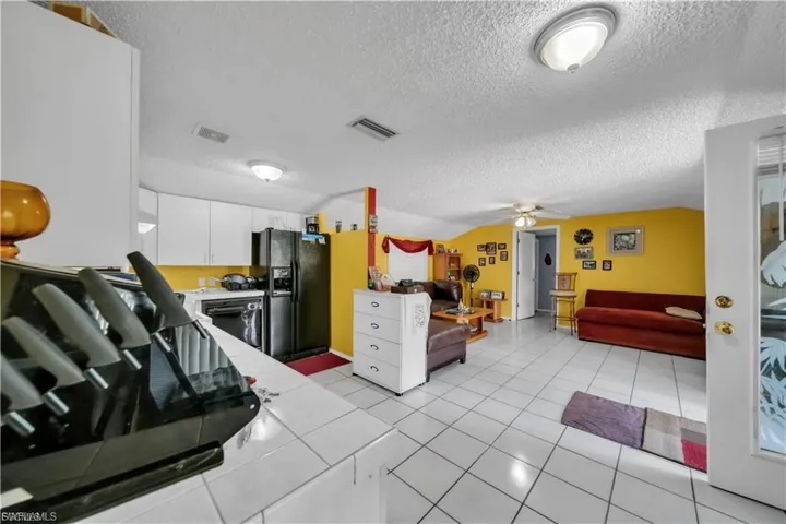 Open-concept living area featuring ceramic tile flooring throughout, stainless steel appliances, white cabinetry, and bright yellow accent walls