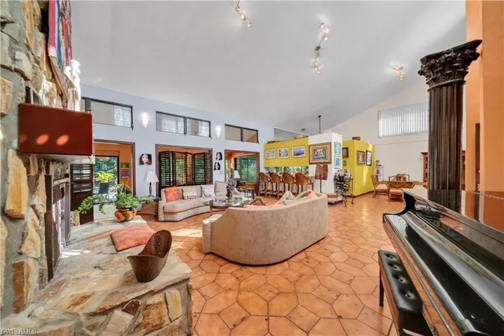 Expansive living area with vaulted ceilings, natural stone fireplace, patterned tile flooring, and track lighting