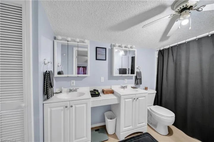 Dual white vanities with integrated sinks, white cabinetry, wall-mounted medicine cabinets with lighting, and a ceiling fan with integrated lighting