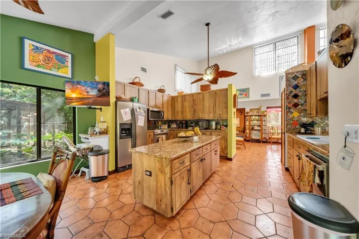 Kitchen featuring wood cabinetry, stainless steel appliances, a central island with a granite countertop, and tiled flooring