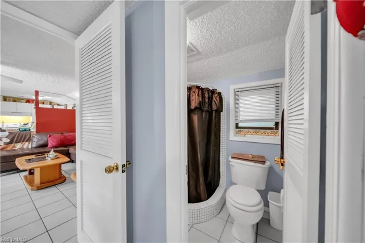 Bathroom featuring a shower with tile surround, a toilet, and a window with blinds
