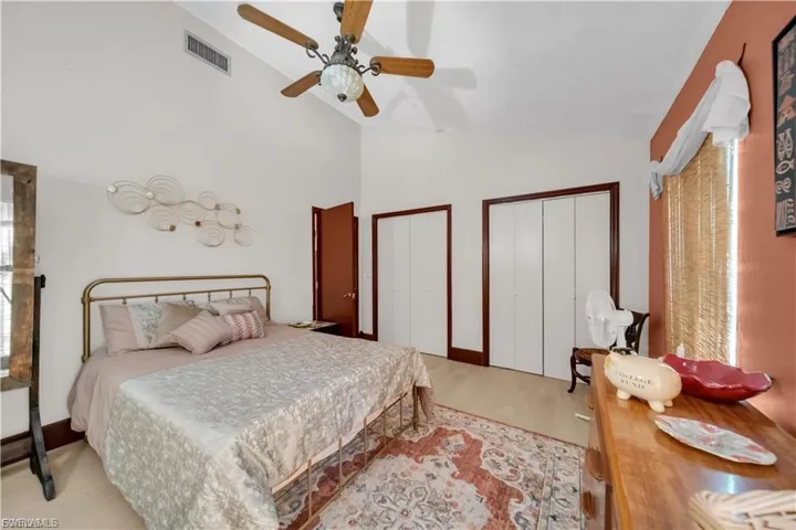 Vaulted ceilings with a ceiling fan, light wood-finish flooring, two sets of bi-fold closet doors, and dark wood trim