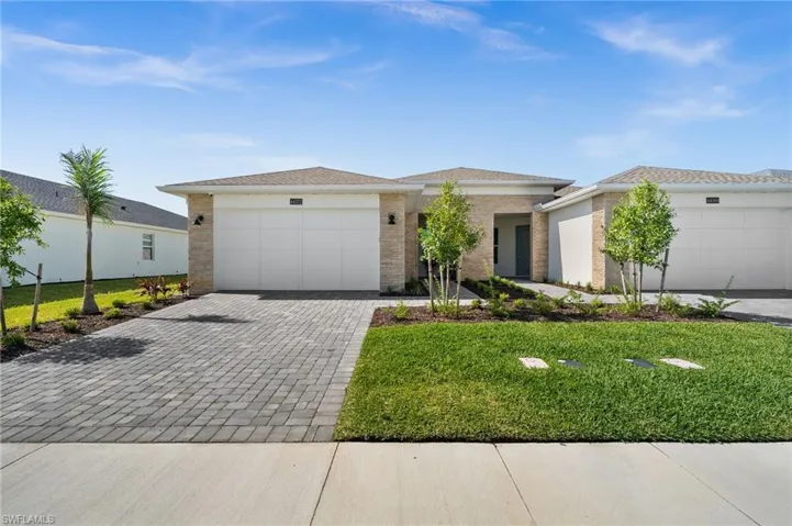 View of front of property featuring an attached garage, brick siding, a front yard, and decorative driveway