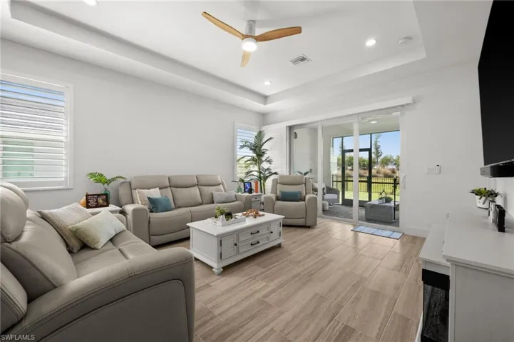 Living area with light wood-type flooring, a ceiling fan, visible vents, recessed lighting, and a raised ceiling
