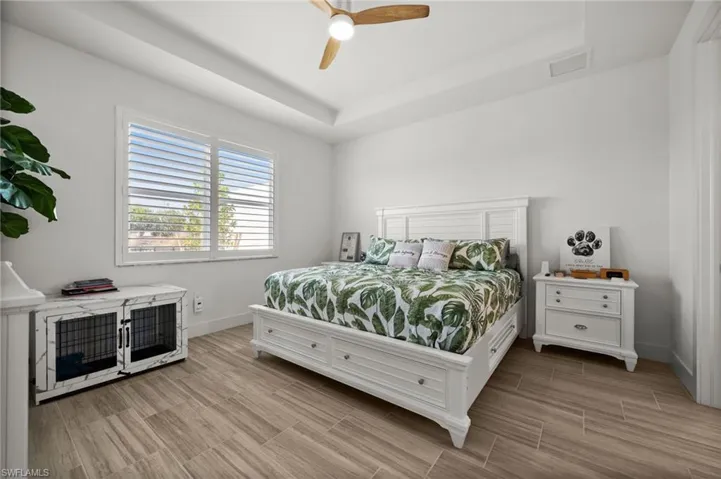 Bedroom with a raised ceiling, light wood-style floors, baseboards, and a ceiling fan