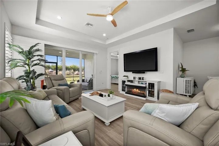 Living room featuring visible vents, a raised ceiling, a ceiling fan, light wood finished floors, and a glass covered fireplace