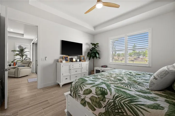 Bedroom with a tray ceiling, baseboards, multiple windows, and light wood finished floors