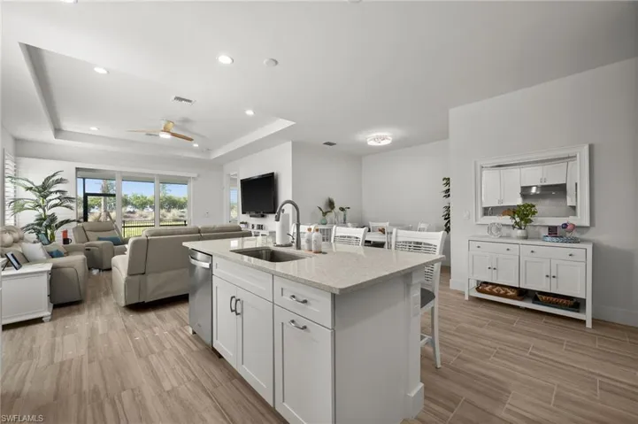 Kitchen with a raised ceiling, a sink, a breakfast bar, a ceiling fan, and white cabinetry