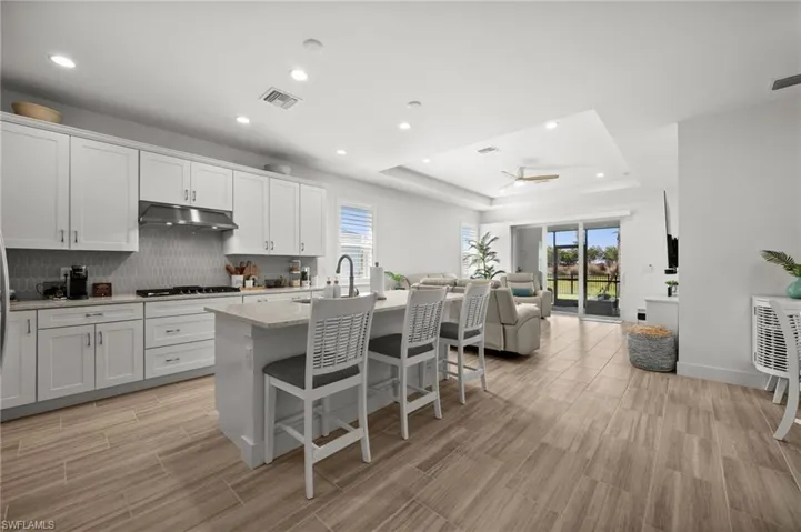 Kitchen featuring open floor plan, under cabinet range hood, visible vents, a tray ceiling, and stainless steel gas cooktop