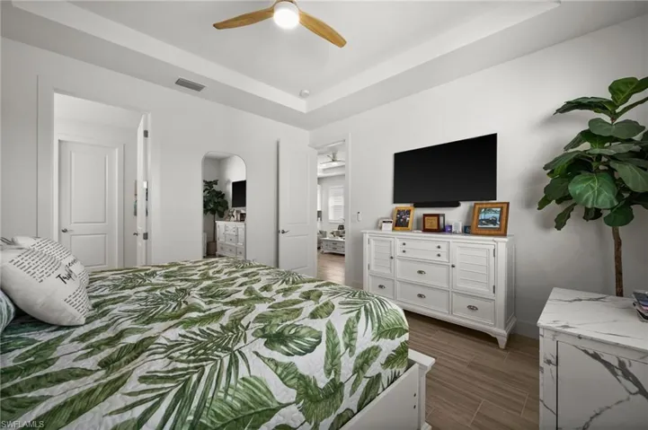 Bedroom with a tray ceiling, arched walkways, visible vents, wood tiled floor, and baseboards