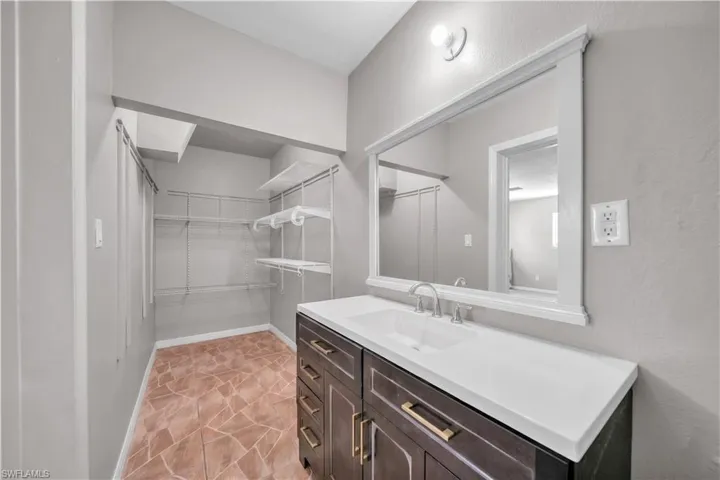 Vanity featuring a single-basin sink, white countertop, and dark wood-finish cabinetry with gold-tone hardware