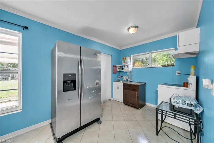 Kitchen featuring a stainless steel side-by-side refrigerator with ice and water dispenser, tile flooring, a wall-mounted range hood, and multiple windows