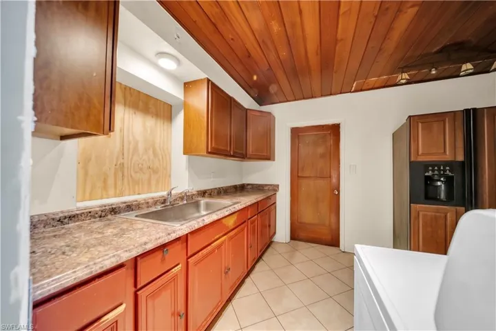 Kitchen featuring wood-paneled ceiling, L-shaped laminate countertops, stainless steel sink, and built-in refrigerator