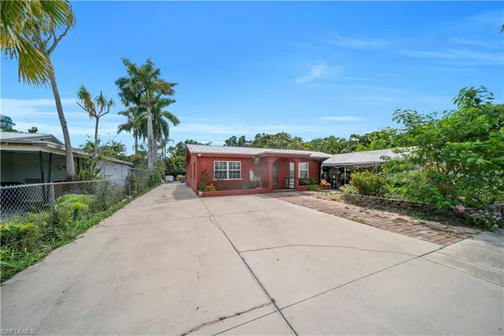 Red-hued exterior featuring a covered porch entry, white-framed windows, and a paved driveway