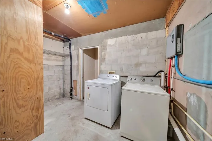 Concrete slab flooring in a utility space featuring a washer and dryer unit, exposed block walls, and visible plumbing lines