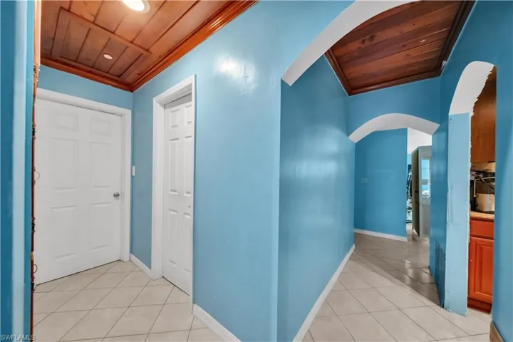 Hallway featuring light blue walls, arched doorways, a wood-finish plank ceiling, and tiled flooring
