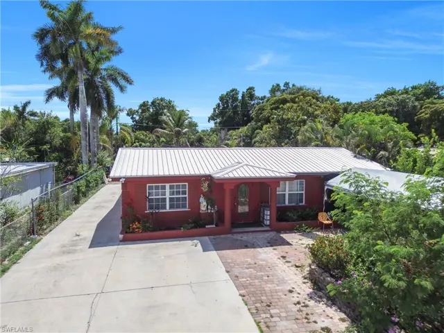 Red-hued residence featuring a white metal roof, a covered porch entry, and white-framed windows