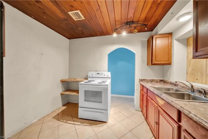Kitchen featuring a wood-panel ceiling, track lighting, an arched doorway, a white electric range, and a double-basin stainless steel sink with a high-arc faucet