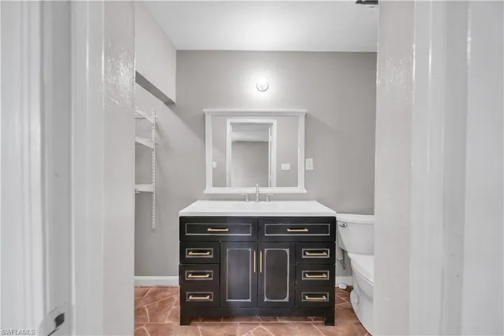 Bathroom featuring a dark wood-finish vanity with gold-tone hardware, a white countertop, and an integrated sink with a chrome faucet