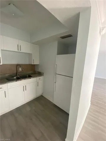 Kitchen with freestanding refrigerator, dark countertops, white cabinets, and dark wood finished floors