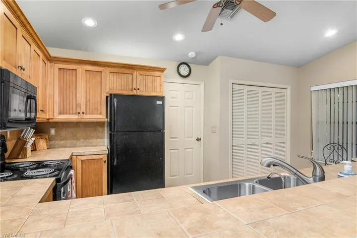 Kitchen with black appliances, tile countertops, ceiling fan, a sink, and decorative backsplash