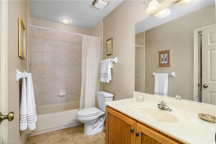 Bathroom featuring toilet, vanity, shower / bathtub combination with curtain, and tile patterned flooring