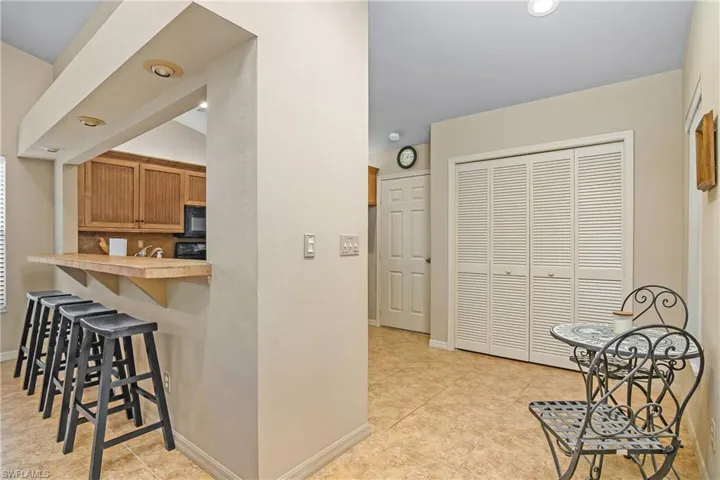 Kitchen featuring a kitchen bar, black microwave, baseboards, light tile patterned floors, and light countertops