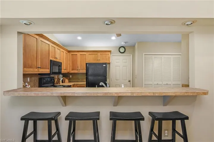 Kitchen featuring black appliances, a peninsula, decorative backsplash, a kitchen bar, and tile counters