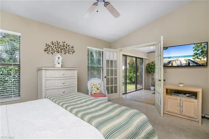 Bedroom with light colored carpet, access to exterior, multiple windows, vaulted ceiling, and a ceiling fan