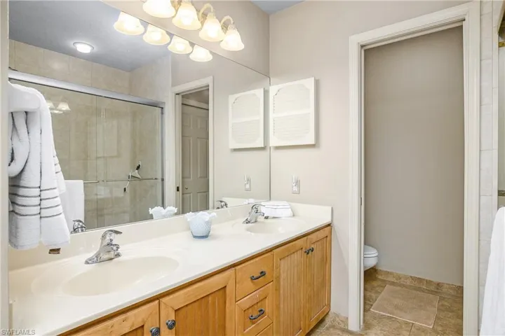 Bathroom with a shower stall, double vanity, toilet, and baseboards
