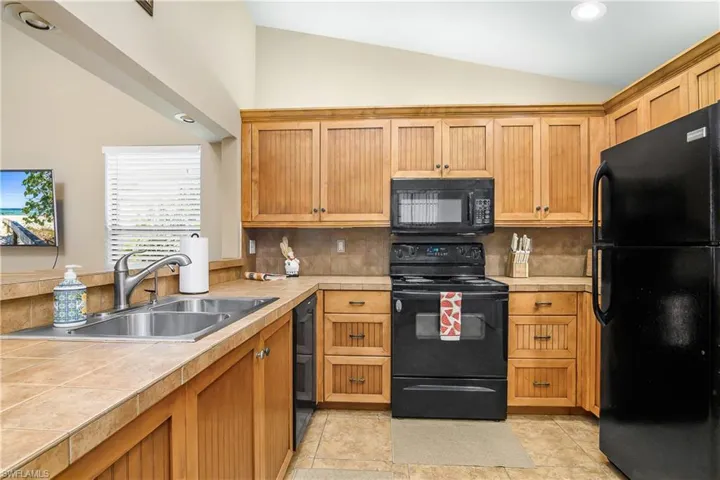 Kitchen featuring black appliances, a sink, decorative backsplash, tile counters, and high vaulted ceiling