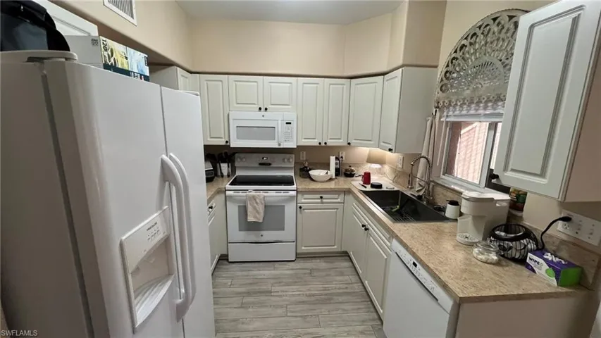Kitchen with white cabinets, light wood-type flooring, white appliances, and sink