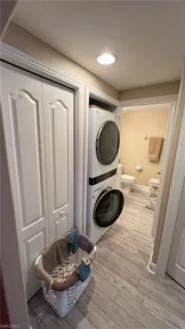 Washroom with light wood-type flooring and stacked washer / drying machine