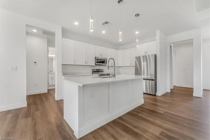 Kitchen with stainless steel appliances, light countertops, wood finished floors, white cabinets, and an island with sink