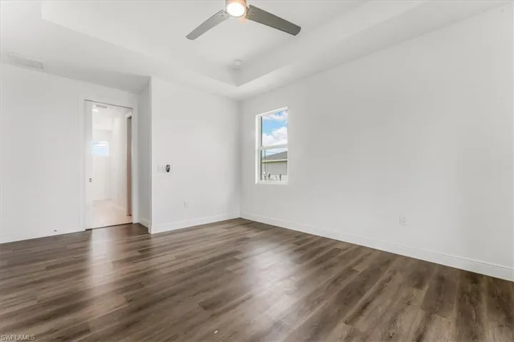 Spare room featuring a raised ceiling, a ceiling fan, and dark wood-style floors
